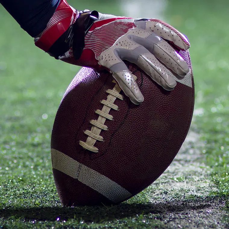 Close-up of a football player's gloved hand placing an American football on the field before kickoff