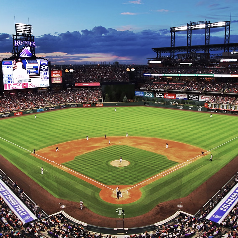 Wide-angle view of a professional baseball game at Coors Field during sunset with full stands and players in action