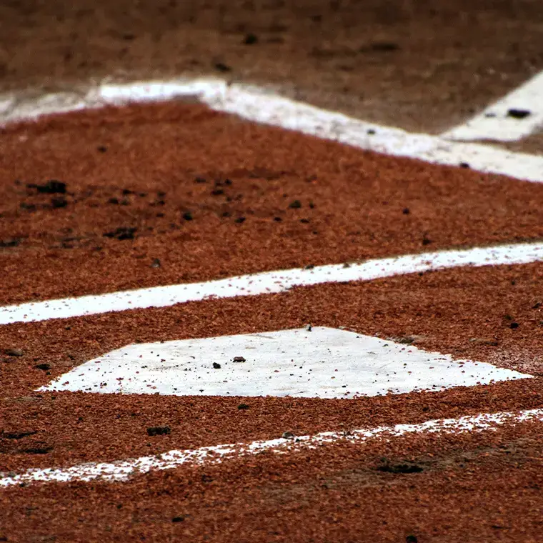 Close-up of a baseball home plate on a dirt field with white chalk baselines