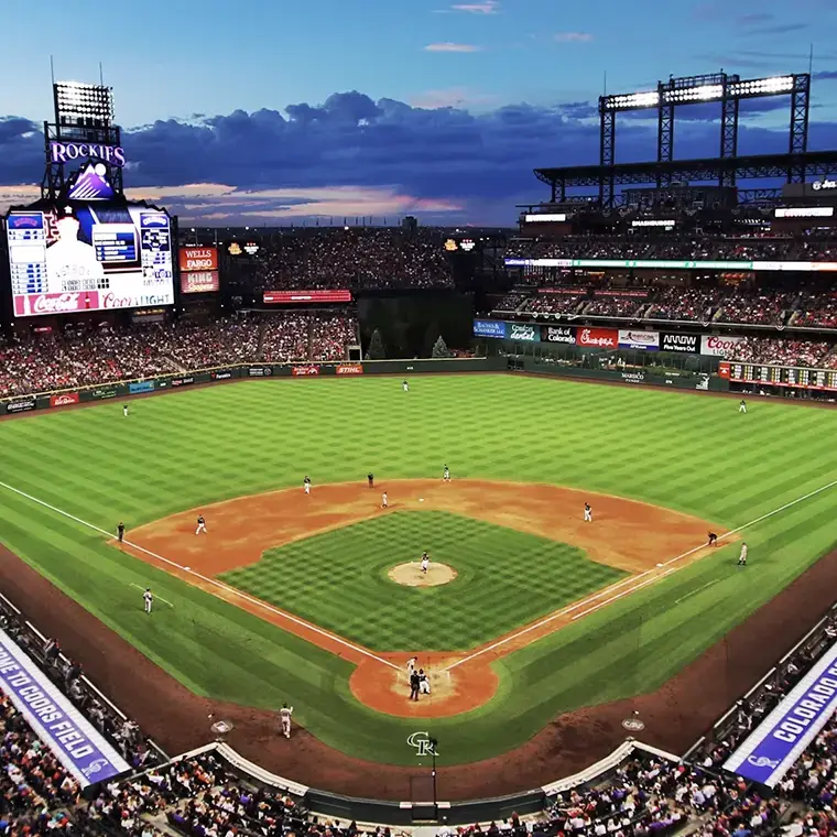 Full stadium view of a live baseball game at dusk with teams on the field and fans in the stands