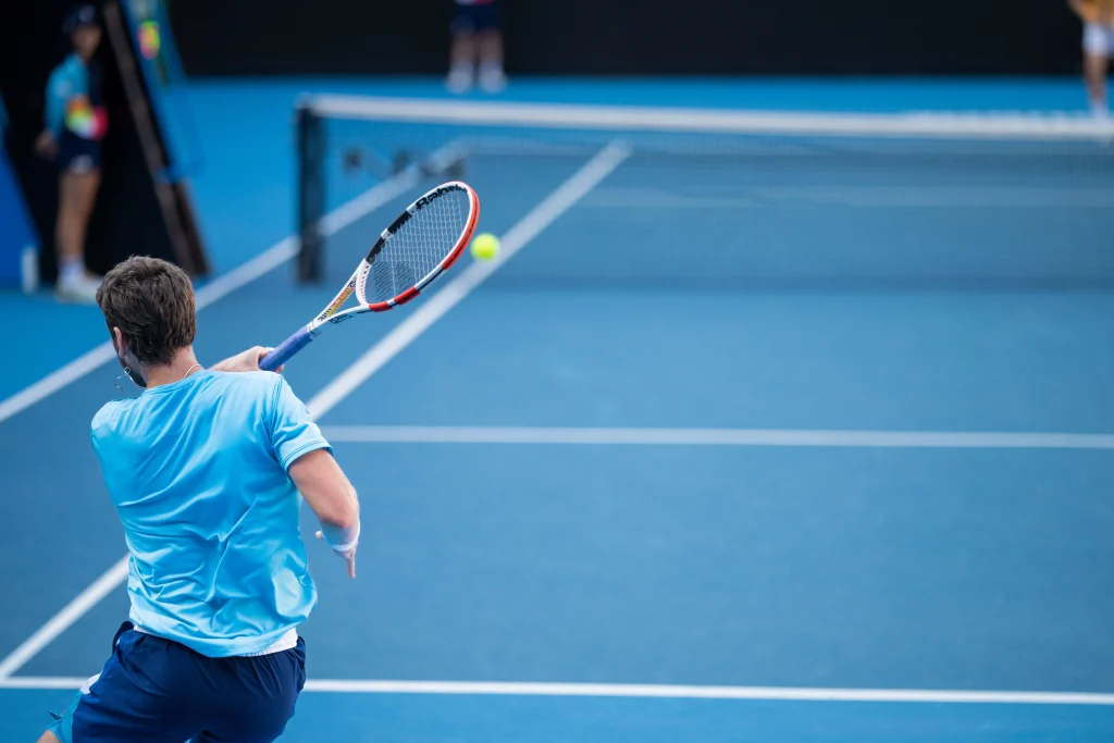 Jugador de tenis con camiseta azul golpeando un golpe de derecha en una cancha dura durante un partido