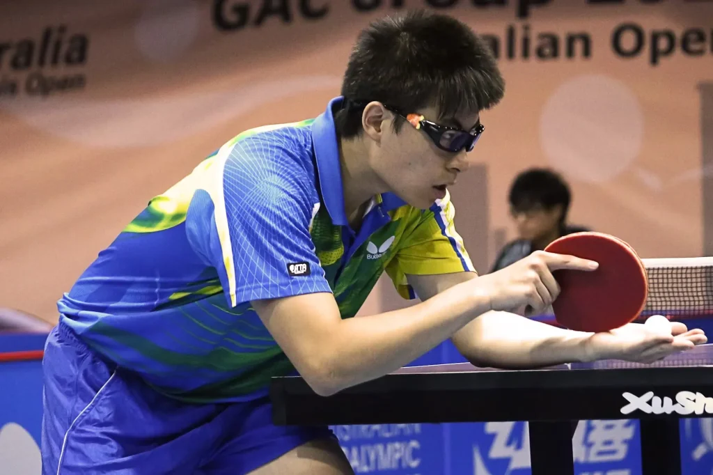Table tennis player in mid-serve, focusing intensely while preparing to strike the ball
